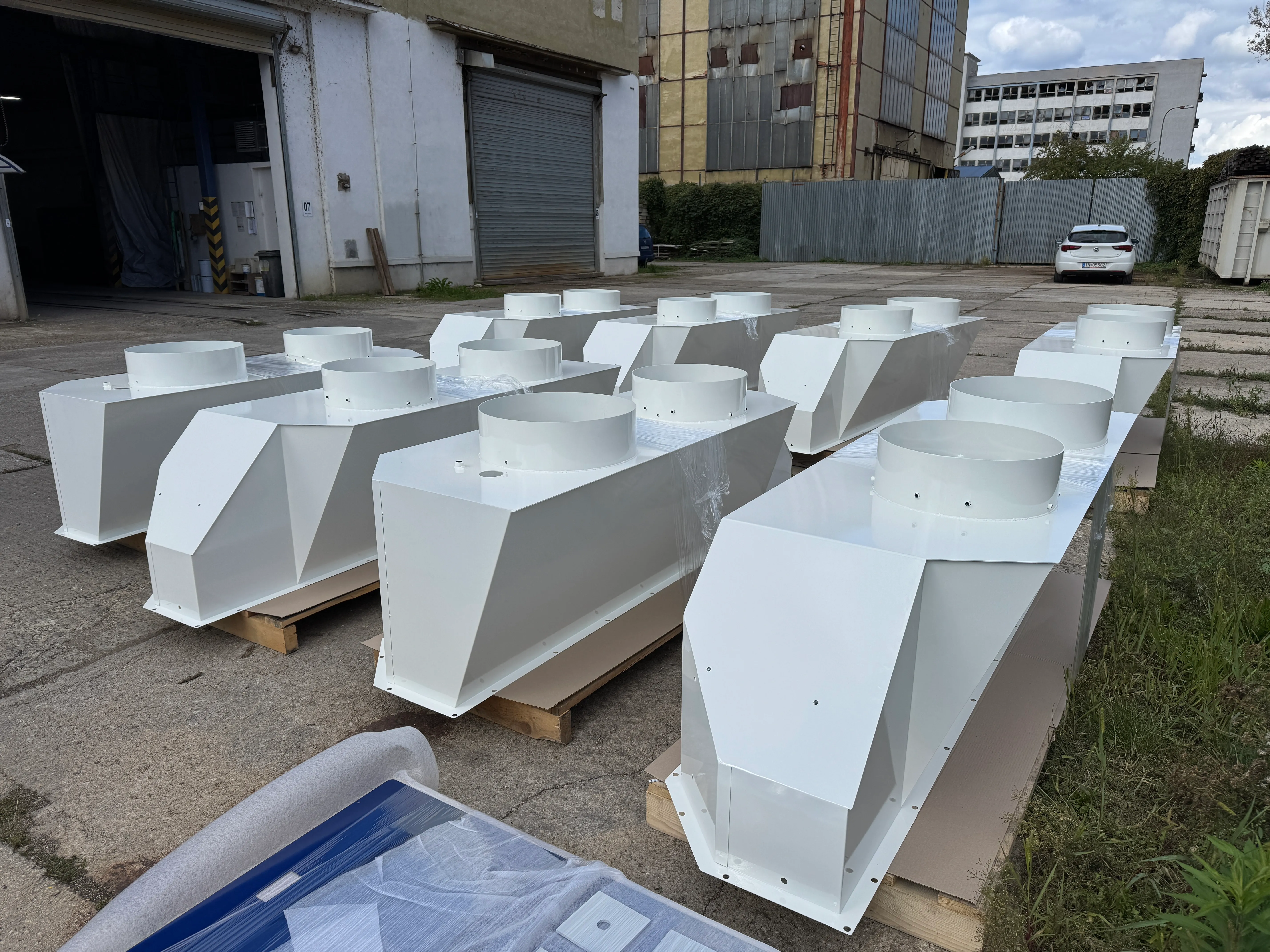 Biele lakované diely uložené na paletách v exteriéri prevádzky.